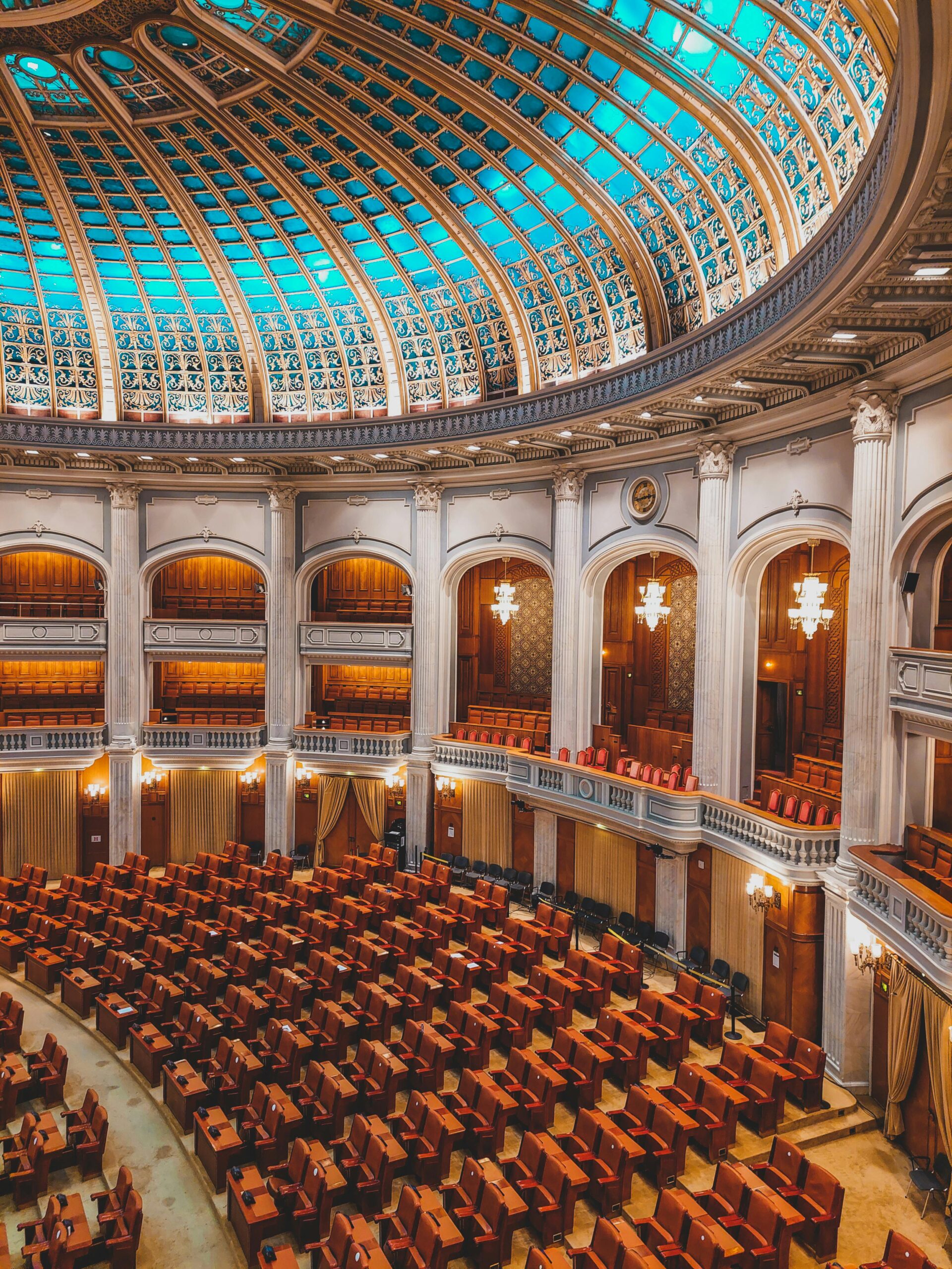 Majestic view of an ornate parliamentary chamber with a striking turquoise dome and plush seating.