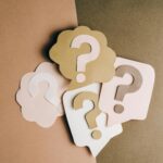 Question mark cutouts in layered paper craft style on a brown backdrop, conceptual art.